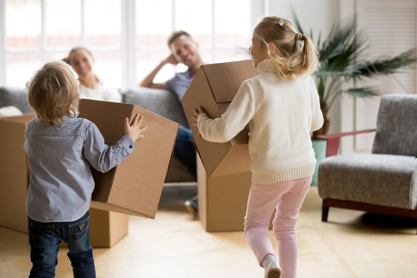 Parents following 3 moving-in tips in their new home while their children hold moving boxes